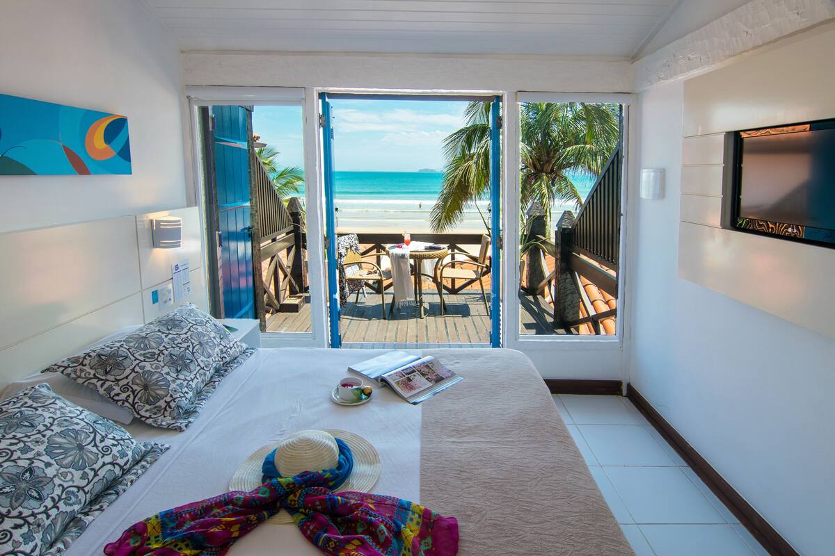 A bedroom with a bed, a TV, and a view of the beach.