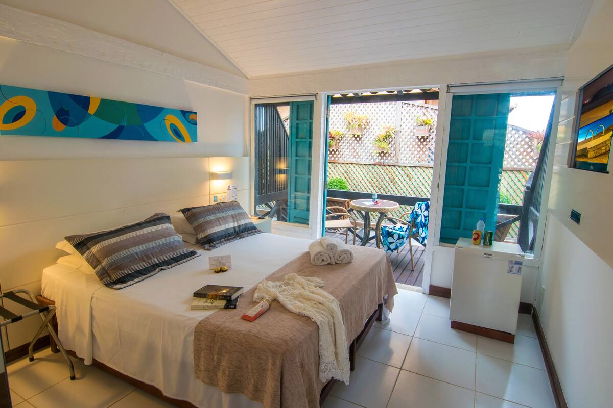 A hotel room with a bed, a small table, a refrigerator, and a view of the outdoor area.