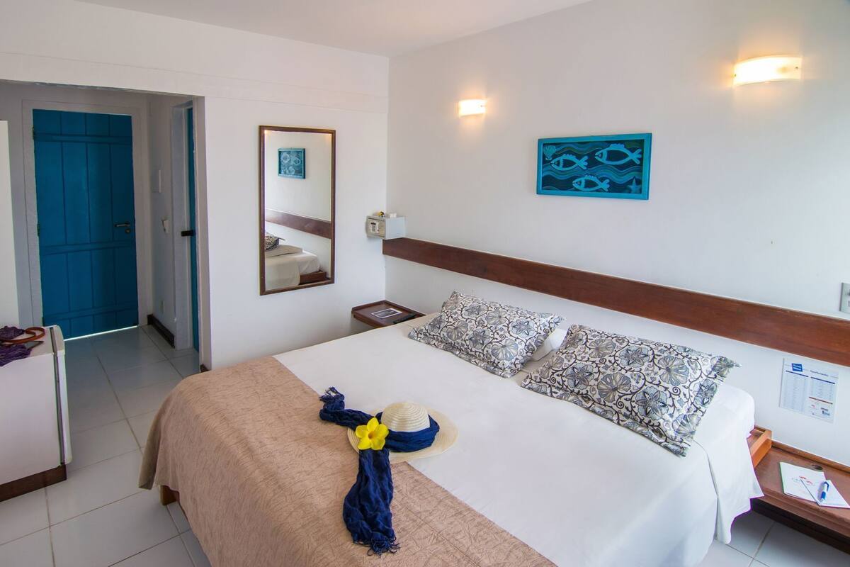 A hotel room with a bed, a bedside table, a mirror, and a wall-mounted light fixture.