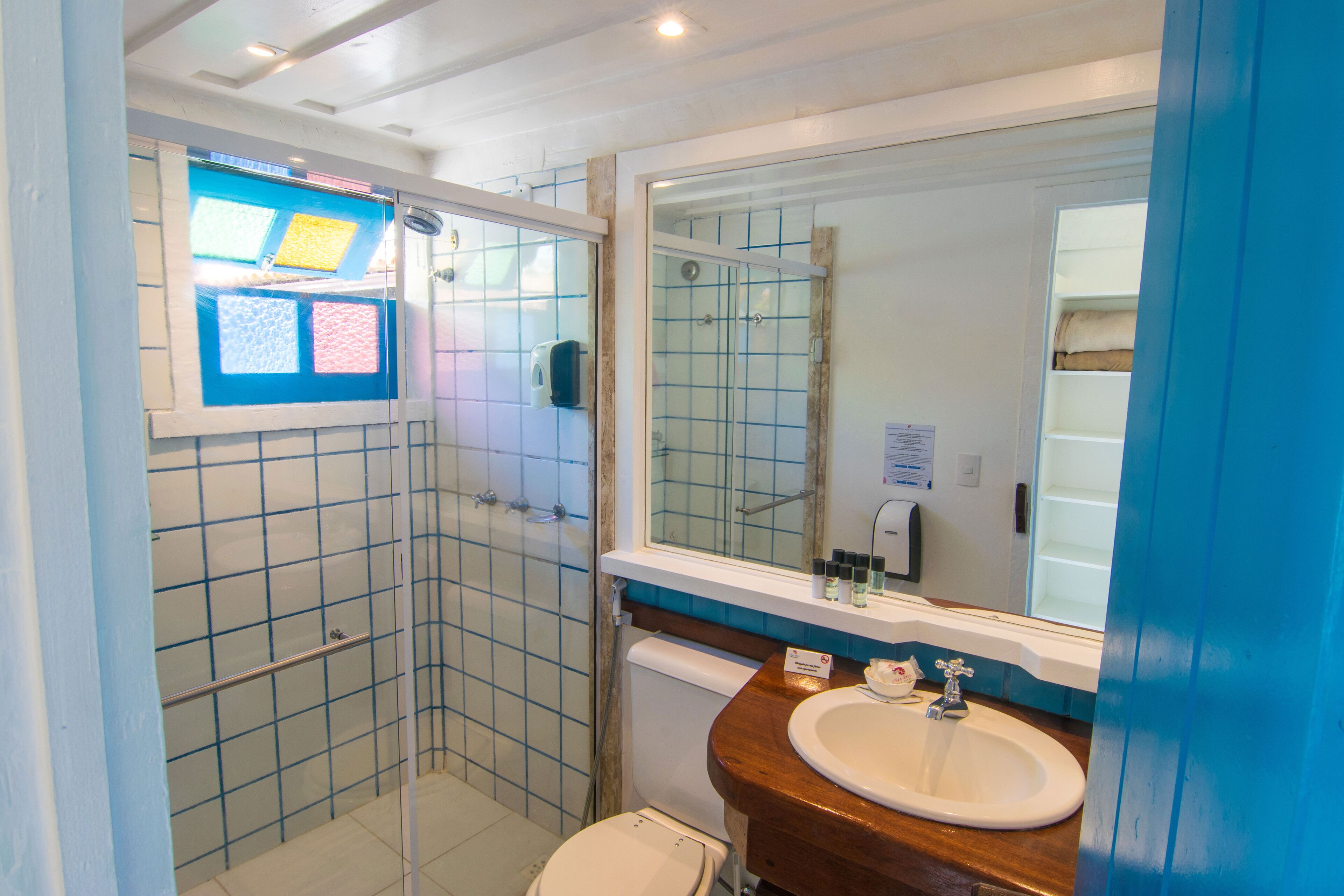 A bathroom with a glass-enclosed shower, a white toilet, a sink with a wooden countertop, and a large mirror.