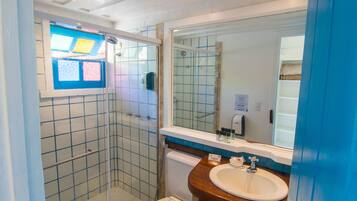 A bathroom with a glass-enclosed shower, a white toilet, a sink with a wooden countertop, and a large mirror.