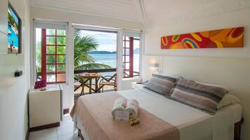 A hotel room with a bed, a view of the ocean, a painting on the wall, and a small table with a chair.