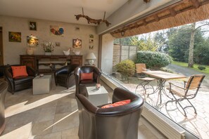 A spacious living area with leather furniture, a dining table, and a view of a garden through large windows.