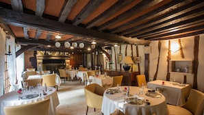 Un restaurante con mesas redondas, sillas y un interior rústico con vigas a la vista y paredes de madera.