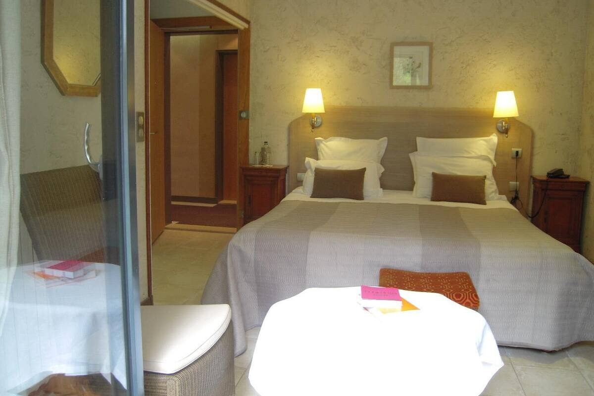 A hotel room with a large bed, two bedside lamps, a nightstand, a chair, a small table, and a mirror.