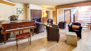 Amplia sala de estar con un piano de cola, asientos cómodos, una mesita y una escalera que lleva a un nivel superior.
