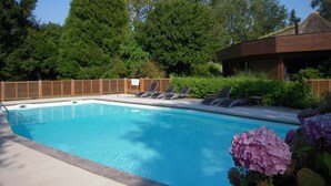 Piscina con sillas de descanso, rodeada de follaje y una valla de madera.