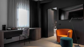Una sala de estar moderna con una pared oscura, un televisor de pantalla plana grande, un sillón naranja brillante, un otoman teal y un escritorio con una silla y una máquina de café.
