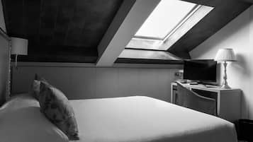 A modern hotel room with a skylight, a bed with a floral pillow, a desk with a lamp, and a television.
