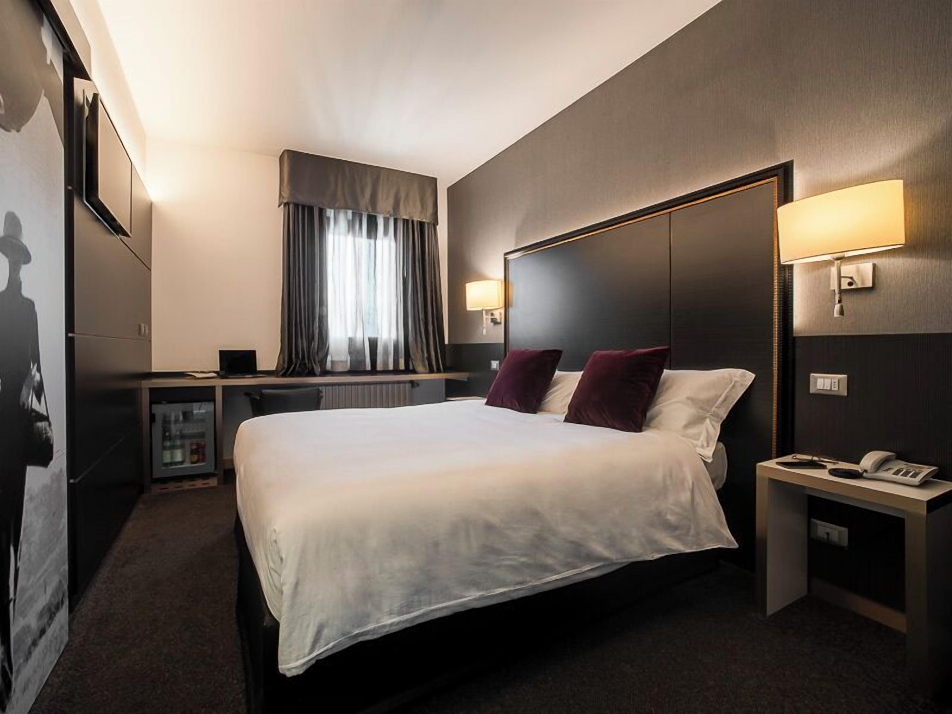 A hotel room with a large bed, bedside lamps, a desk, and a window with curtains.
