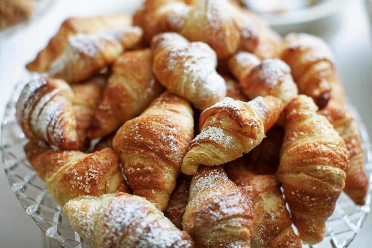 Eine Glasbowl gefüllt mit goldbraunen Croissants, bestäubt mit Puderzucker.