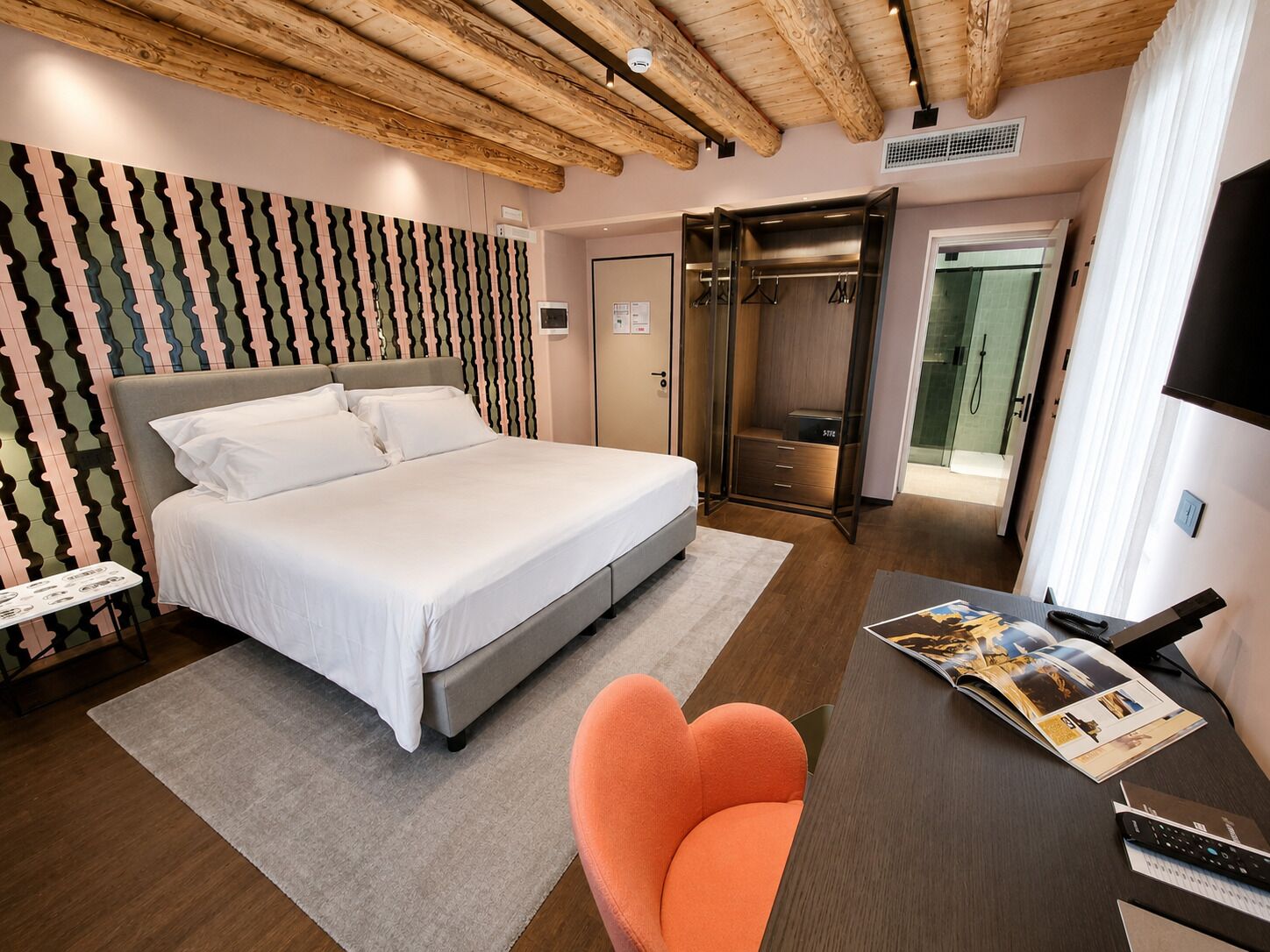 A bedroom with a bed, a desk with a chair, a wardrobe, and a shower area.
