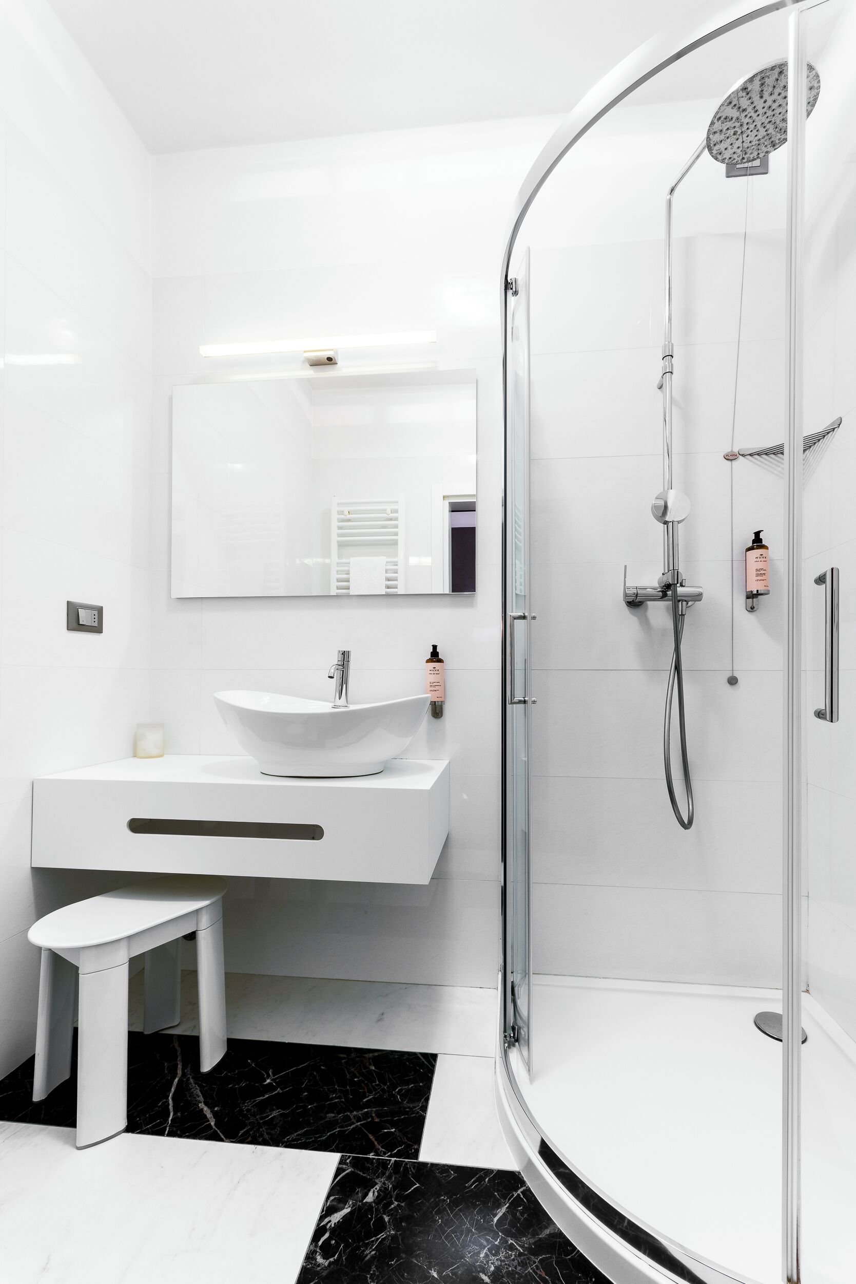 Une salle de bain moderne avec une douche à parois de verre, un meuble-lavabo blanc et un petit tabouret.