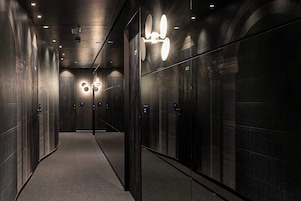 Un hall de ascensores moderno con paredes espejadas, una lámpara central y pantallas digitales en las puertas.