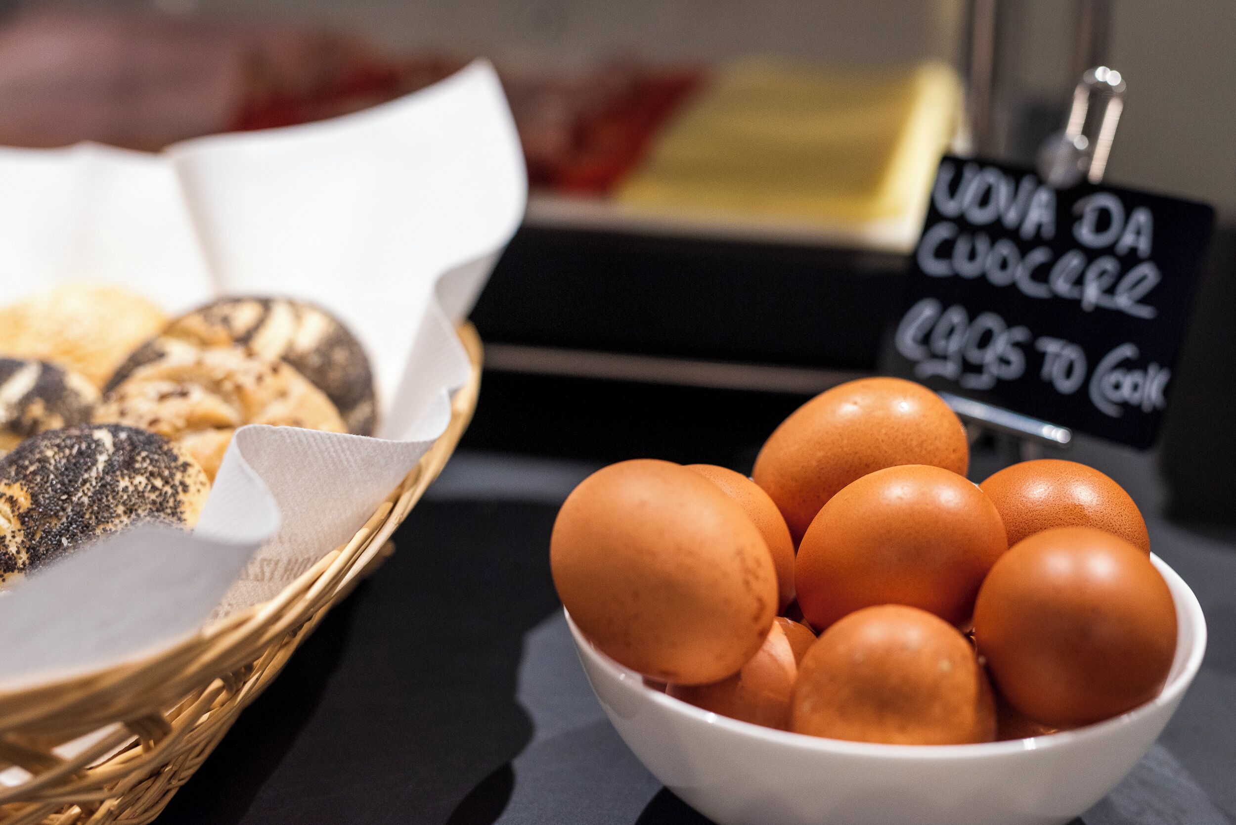 A basket of bread and a bowl of eggs on a table with a sign in the background.