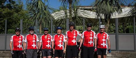 A group of cyclists in red and white uniforms standing in front of a building with palm trees in the background.
