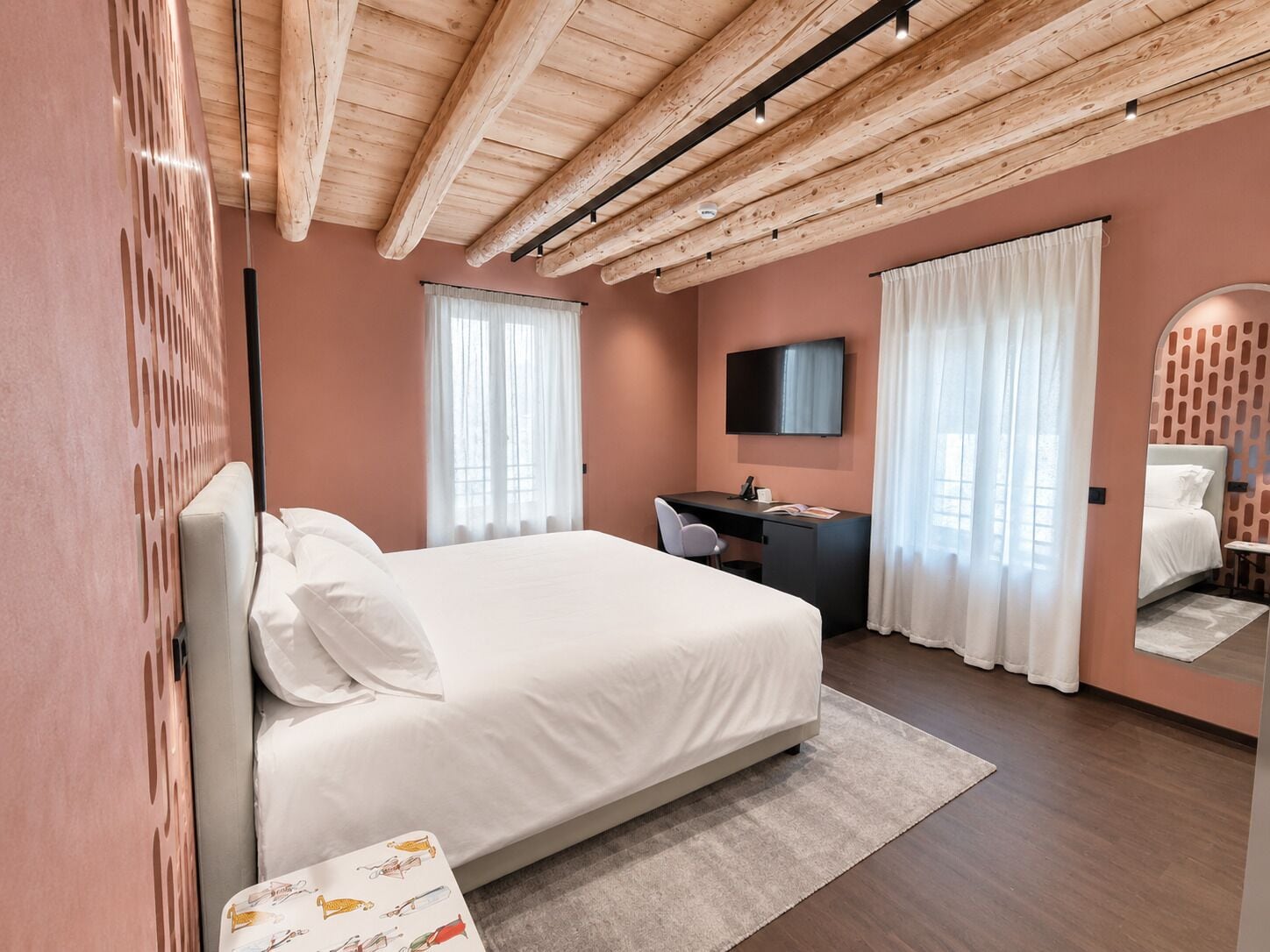 Ett modernt hotellrum med ett träpanelat tak, en stor säng, ett skrivbord, en tv och en spegel.