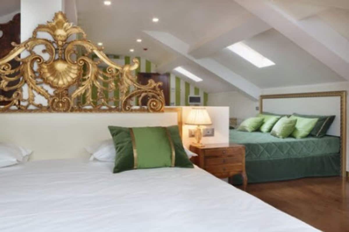 Un dormitorio con una cama grande, una mesita de noche, una lámpara y una cabecera tapizada en verde al fondo.