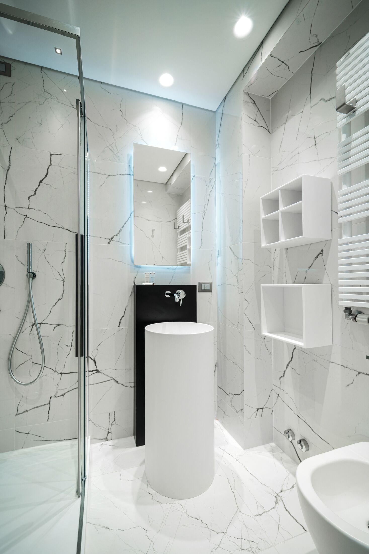 A modern bathroom with a glass shower enclosure, a large white sink, and marble-patterned walls.