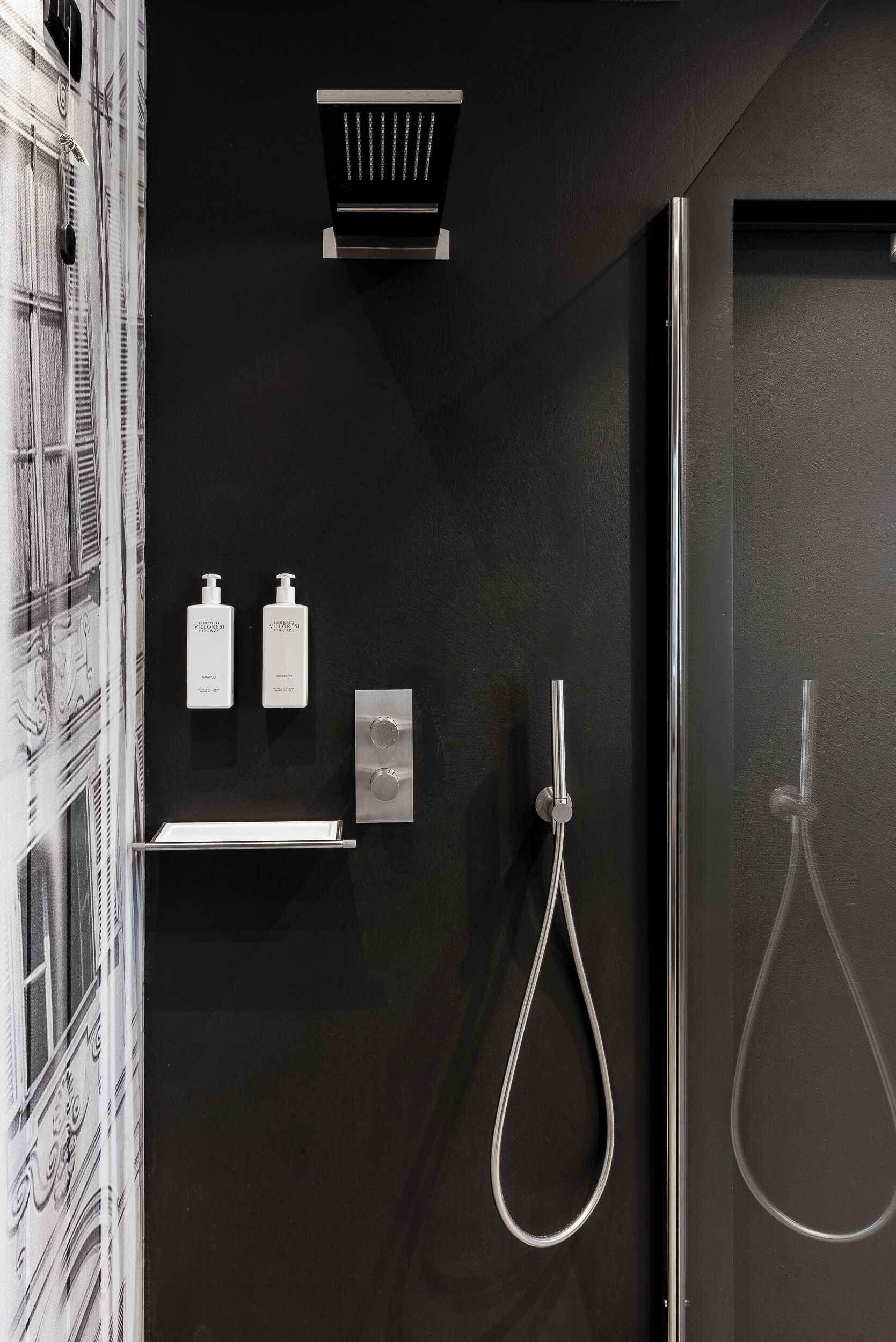 Un baño moderno con una pared negra, una ducha con cabezal de ducha manual y dos botellas de champú y acondicionador sobre un estante.