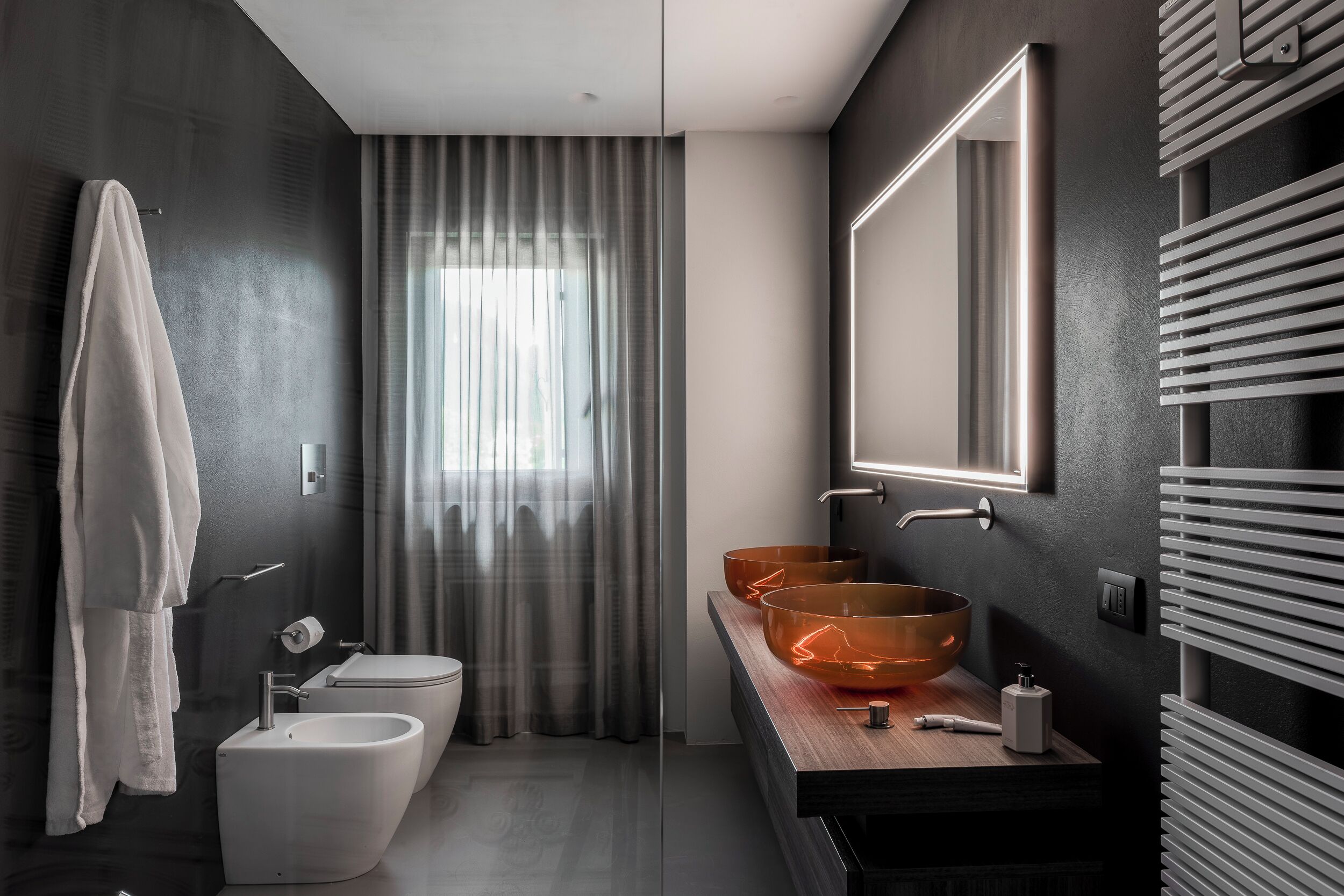 A modern bathroom with a large mirror, two sinks, a bidet, and a towel hanging on the wall.