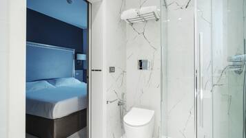 Un bany modern amb una cabina de dutxa de vidre, un vàter blanc i un llit amb el capçal blau.