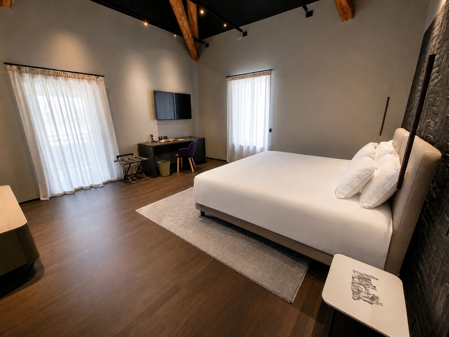 A modern bedroom with a large bed, a desk, and a TV.