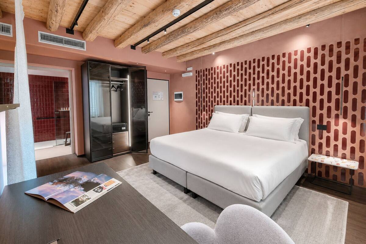 Una habitación de hotel moderna con una cama grande, un escritorio con una revista, un armario y zona de ducha.