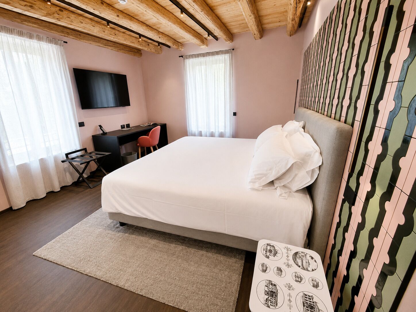 A bedroom with a bed, desk, chair, TV, and patterned wall.