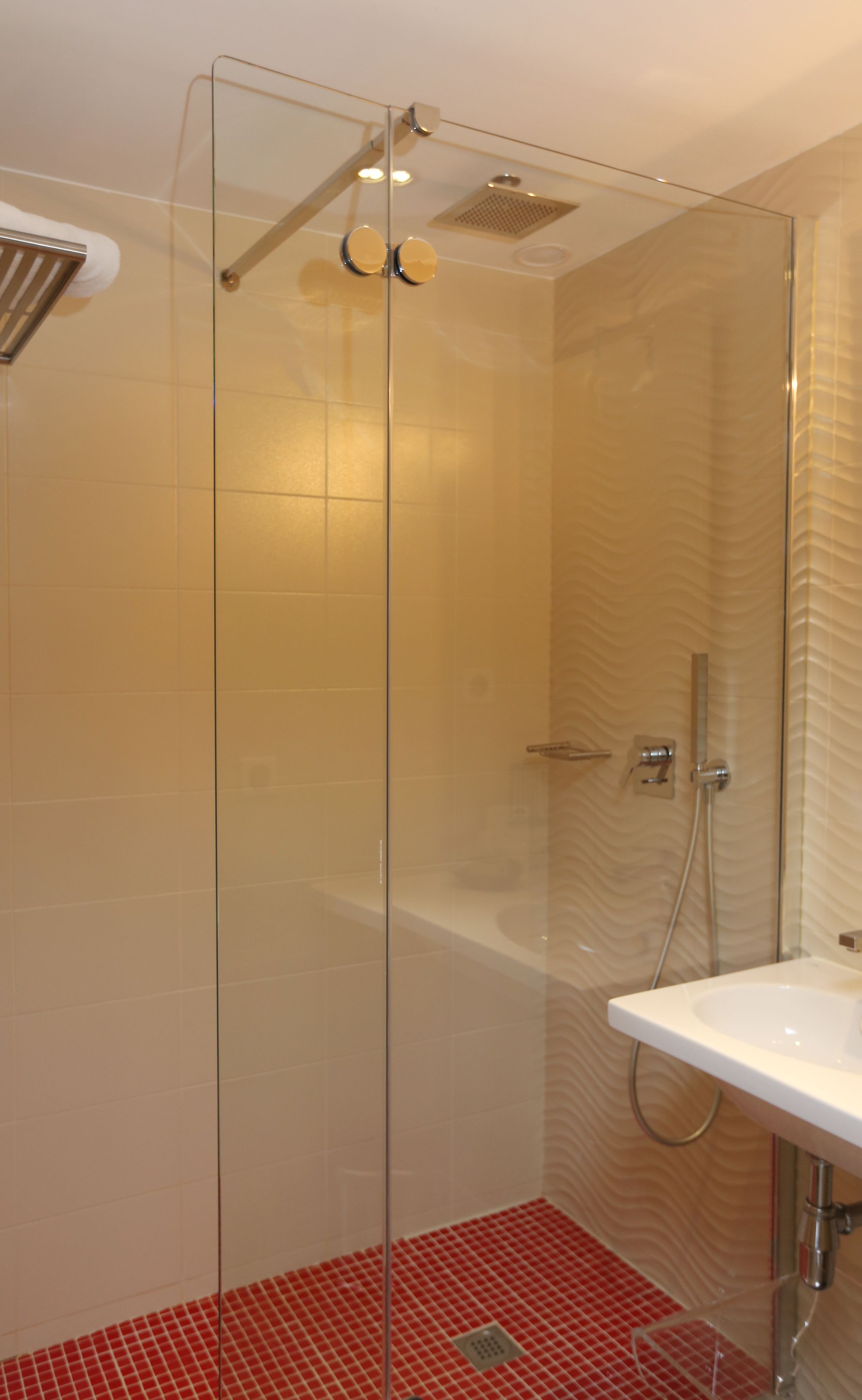 Une salle de bain moderne avec une douche à l’italienne en verre, un lavabo blanc et un sol carrelé de couleur rouge.