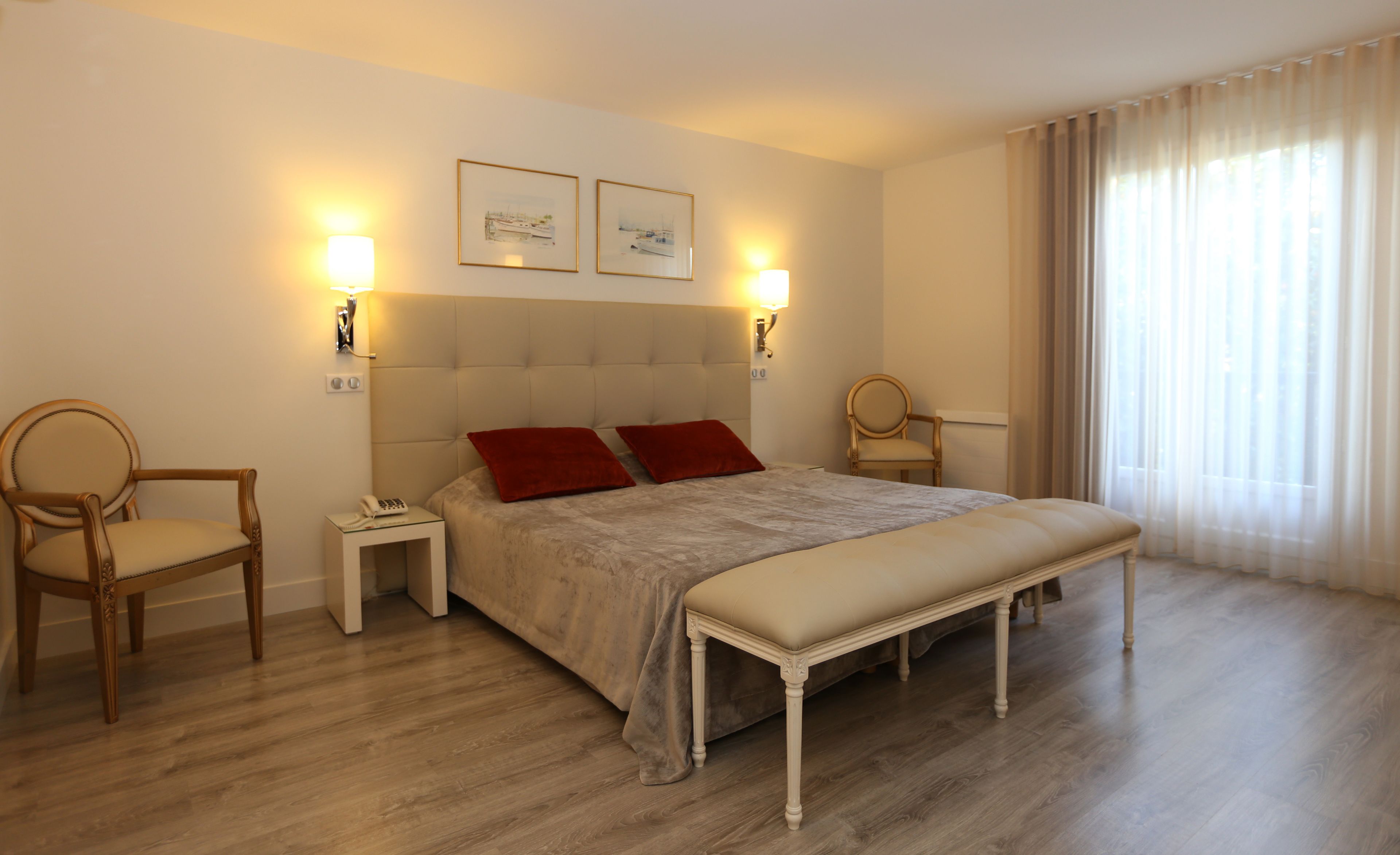 Una habitación de hotel con una cama grande, dos mesitas de noche, una silla y un banco.