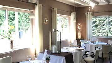 Un restaurante con mesas redondas, sillas y vistas a zonas verdes a través de amplios ventanales.