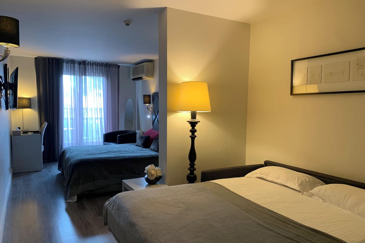 Une chambre d’hôtel avec un grand lit, un lit plus petit, un bureau avec une chaise, une lampe et un climatiseur fixé au mur.
