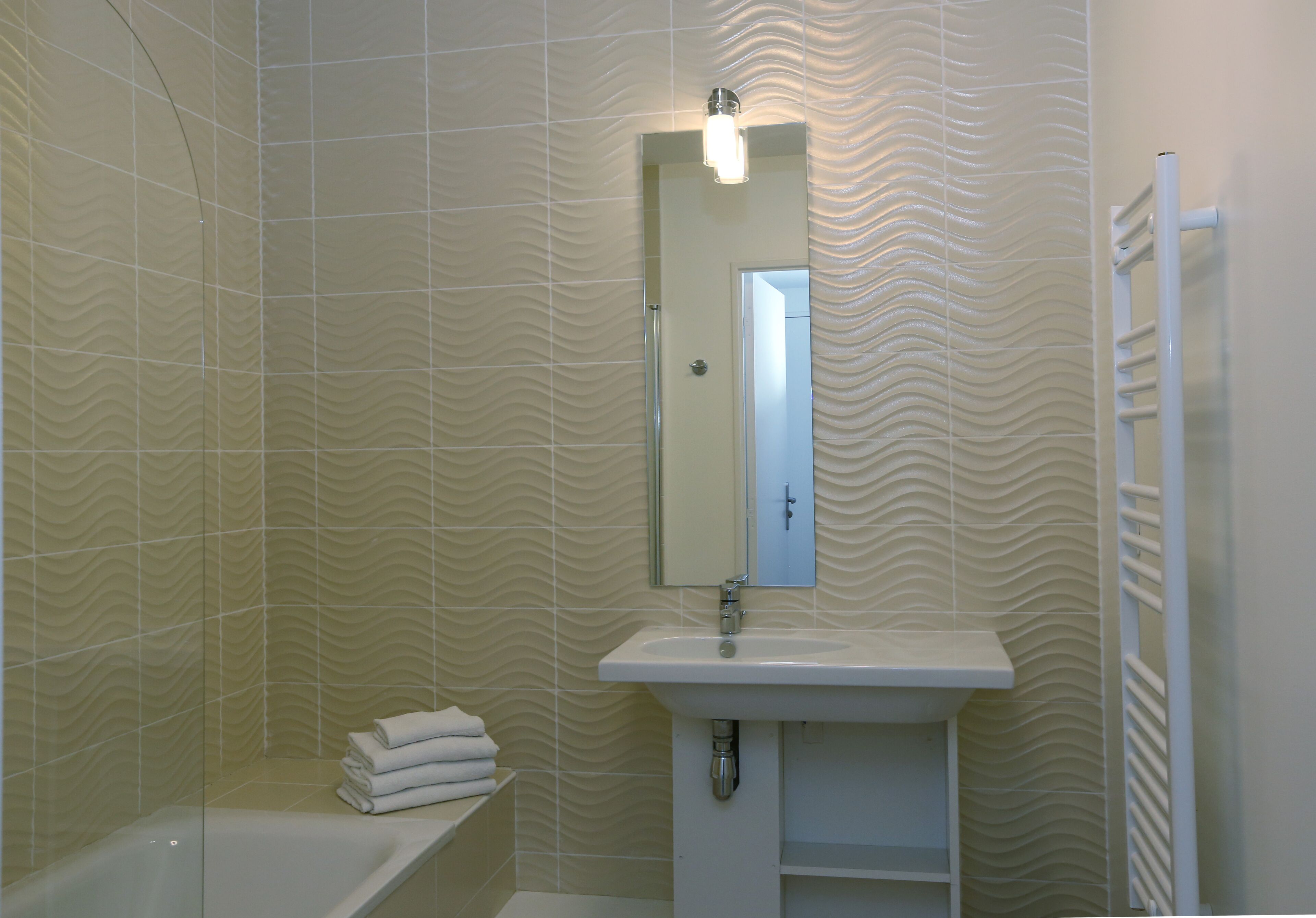 Un baño con bañera, lavamanos con espejo y toallero.