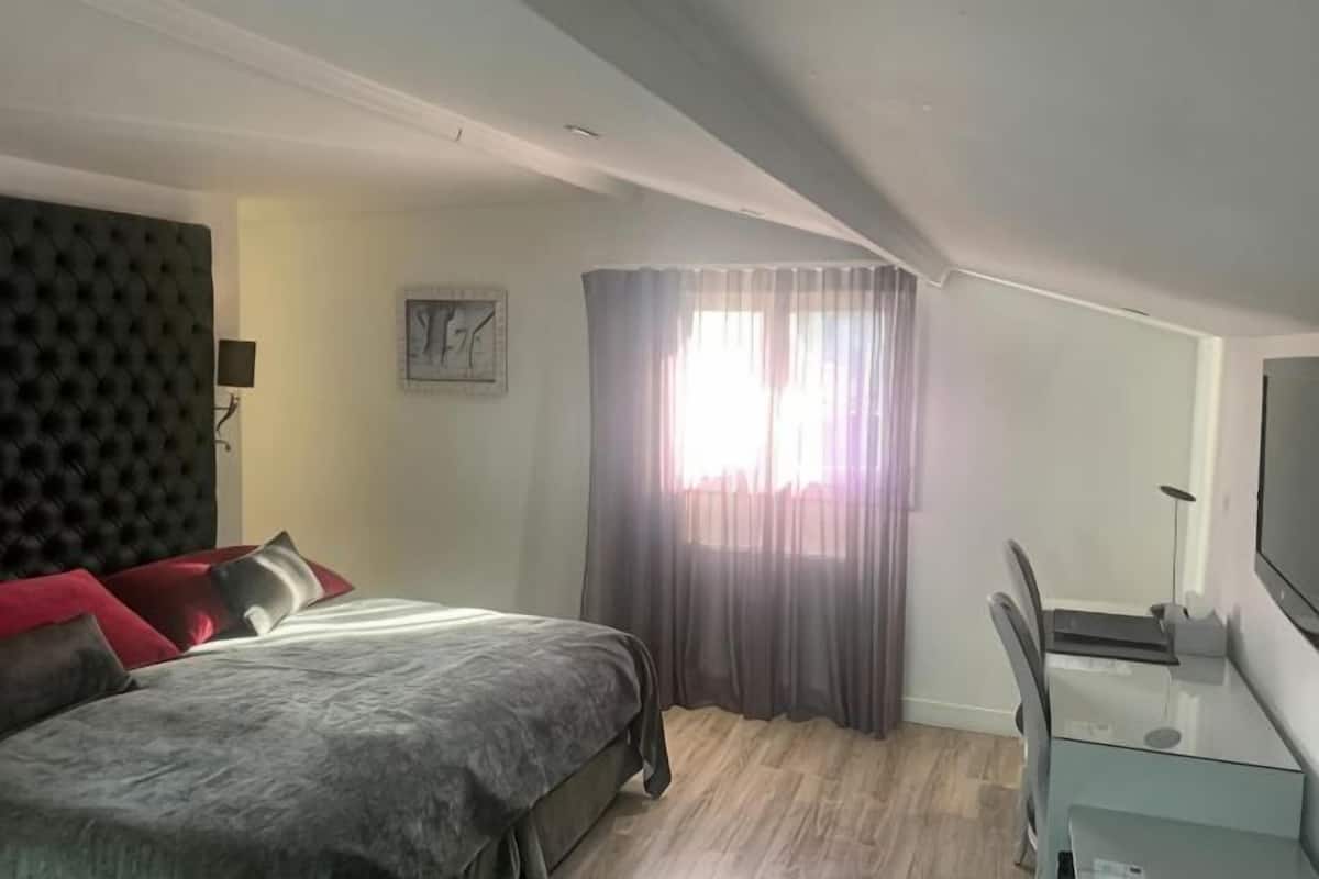 Une chambre à coucher comprenant un lit, un bureau, une chaise, une télévision, une fenêtre avec des rideaux et une horloge au mur.
