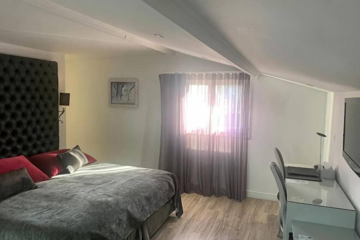 Une chambre à coucher comprenant un lit, un bureau, une chaise, une télévision, une fenêtre avec des rideaux et une horloge au mur.
