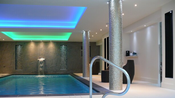 Una piscina interior con pared de vidrio, una bañera de hidromasaje y un pasamanos metálico.