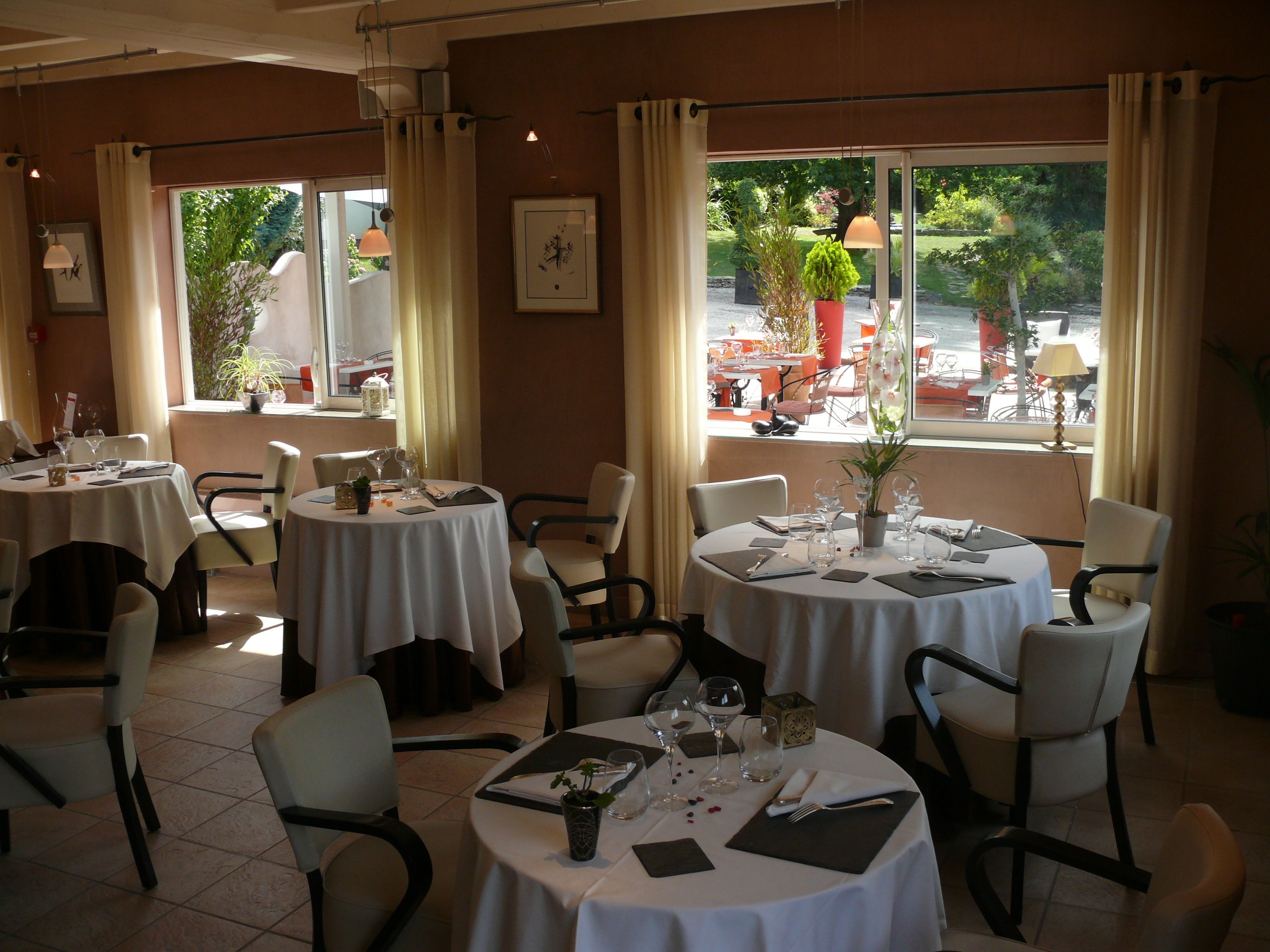 Un restaurante con varias mesas redondas, cada una con mantel blanco, sillas y lo necesario para comer.