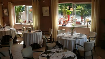 Un restaurante con varias mesas redondas, cada una con mantel blanco, sillas y lo necesario para comer.