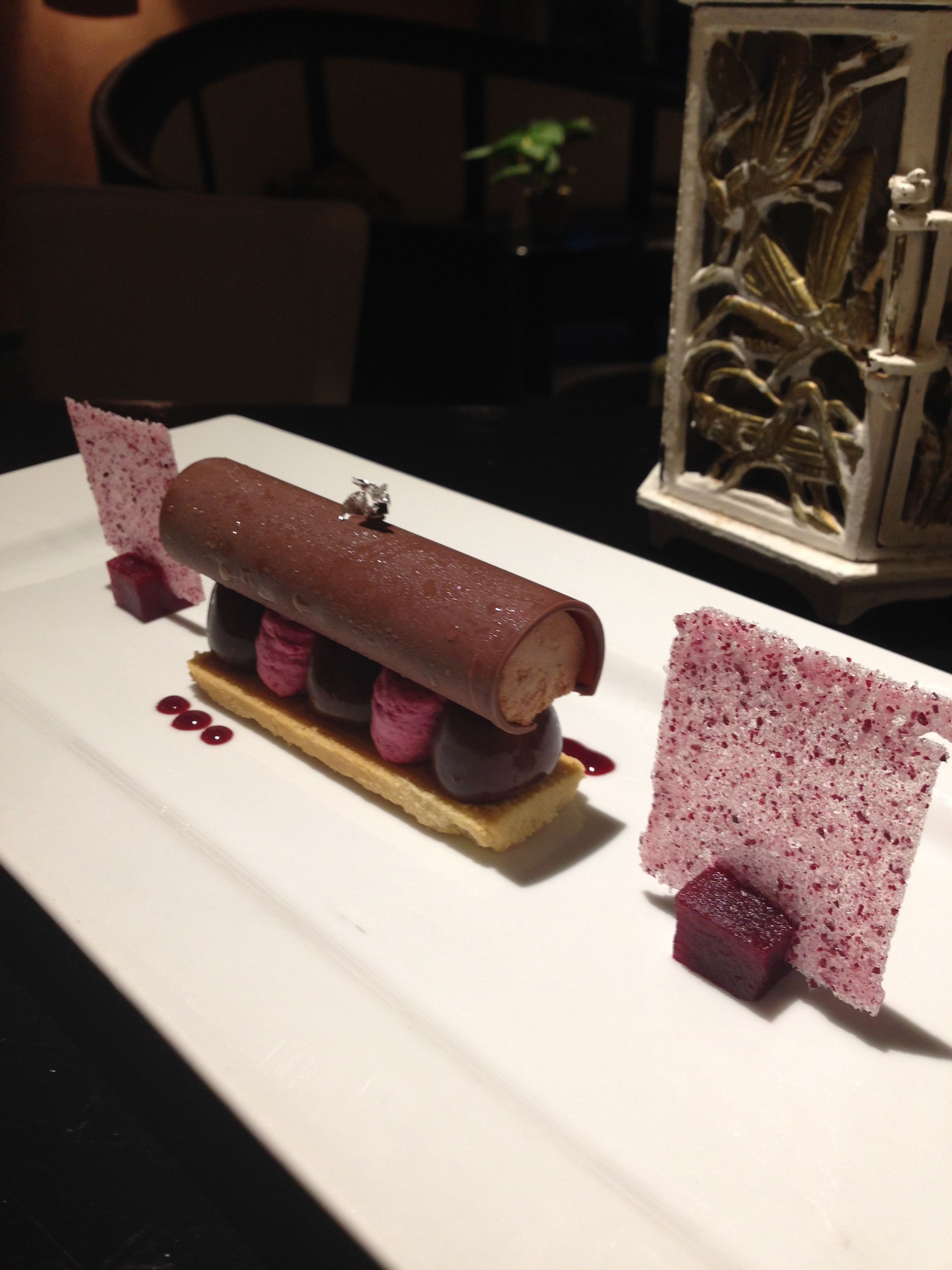Un postre en un plato blanco con un rollo de chocolate, bayas y un adorno.