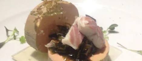 A dessert on a white plate with a square base, garnished with green leaves and a pink element.