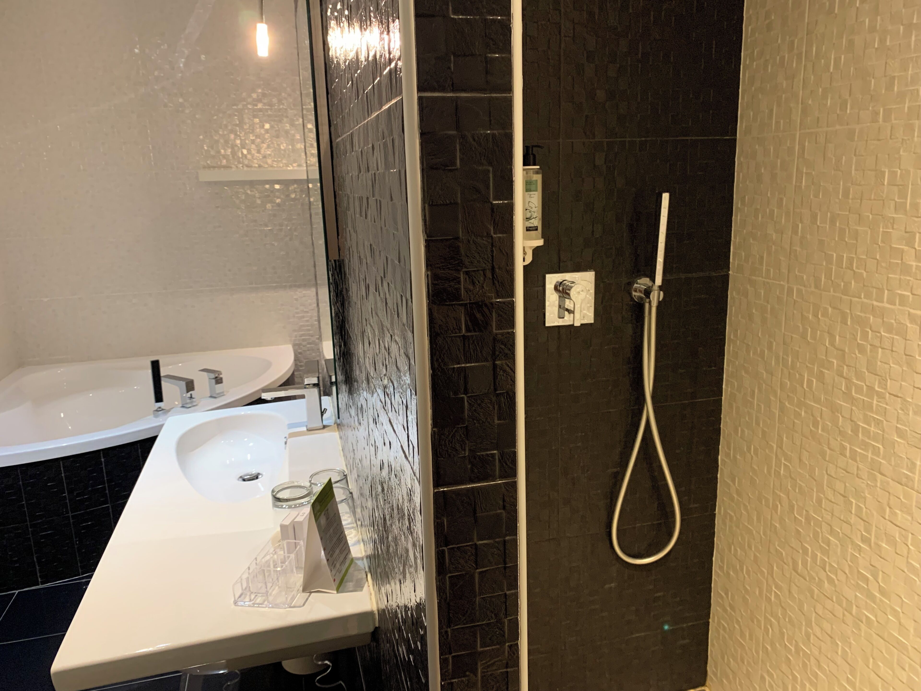 A bathroom with a white sink, a mirror, and a shower area with a handheld showerhead.