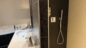 A bathroom with a white sink, a mirror, and a shower area with a handheld showerhead.