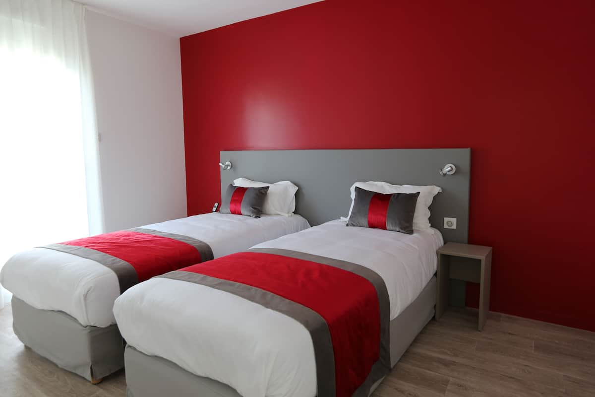 Une chambre d’hôtel avec deux lits, des murs rouges et une petite table de chevet.