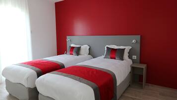 Une chambre d’hôtel avec deux lits, des murs rouges et une petite table de chevet.