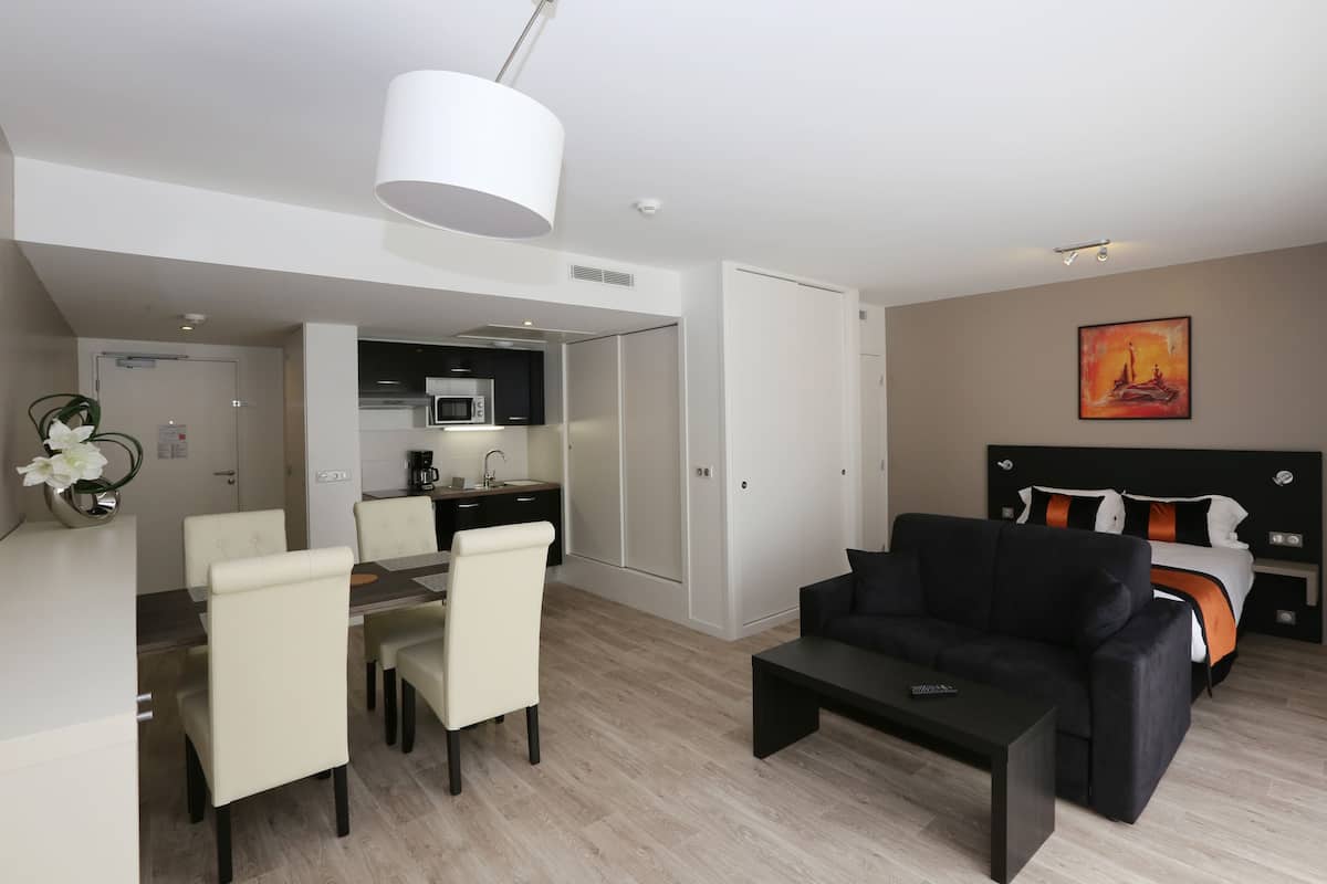 Une chambre d’hôtel moderne avec un coin repas, un canapé noir et un lit doté d’une tête de lit.