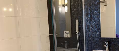 A modern bathroom with a glass-enclosed shower, a white sink, and a tiled floor.