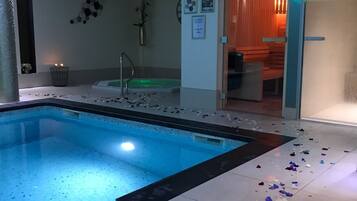 An indoor swimming pool with a black and white tiled floor, surrounded by walls with framed pictures and a door leading to another room.