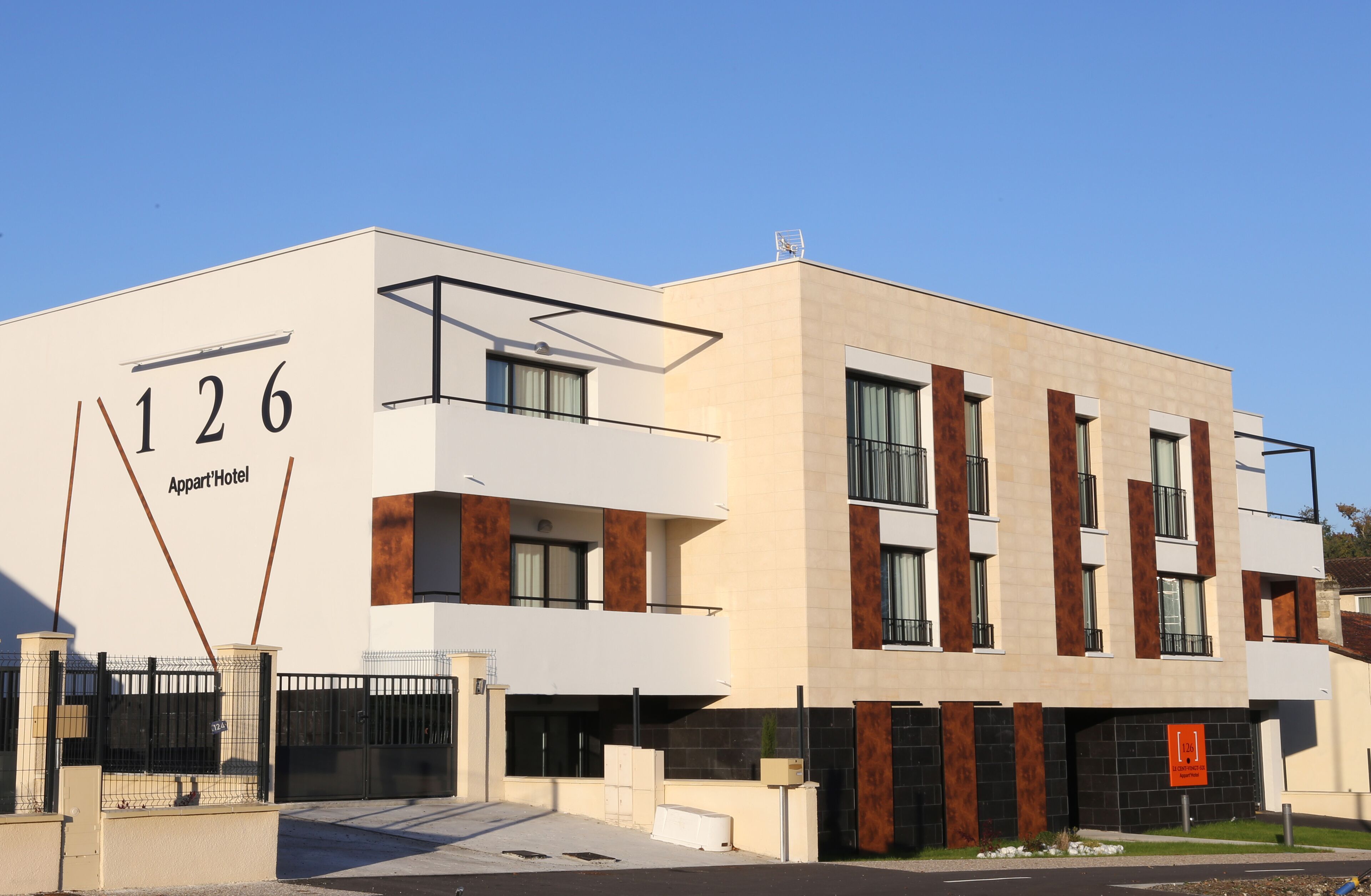 Un hotel moderno con fachada plana, número 126, que presenta una combinación de paneles blancos y marrones, ventanas grandes y una entrada porticada.