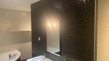 A modern bathroom with a white sink, a large mirror, and dark tiled walls.